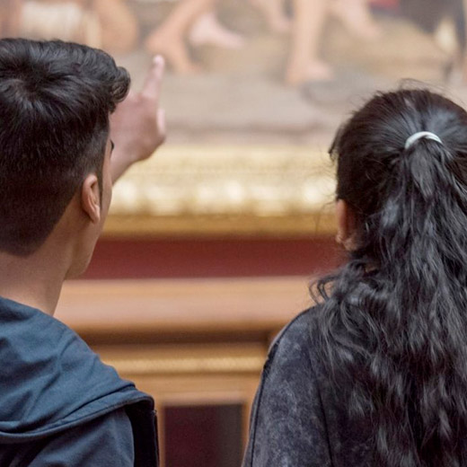 close up of two people from behind, looking and pointing at a painting