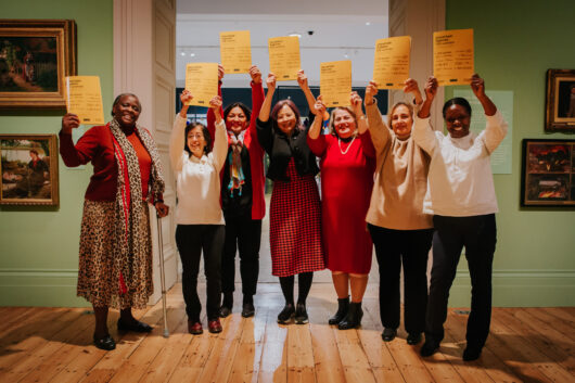 Seven women from the Uncertain Futures project smiling an holding up copies of the report in the gallery
