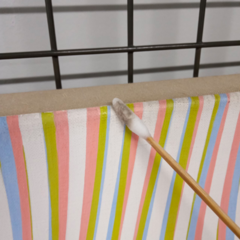 detail of Bridget Riley's Zephyr being cleaned, the painting is striped white, pink, green and blue. A cotton bud shows the dirt removed from the painting
