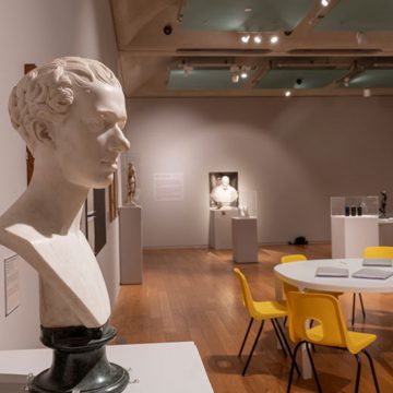 Bust of a male head on left hand side of image, in exhibition/ research room, a table is set with books and chairs placed around it