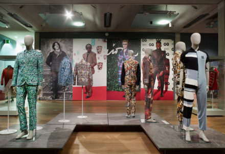 Dandy Style Exhibition view of gallery 13, contemporary suits on mannequins in front of a back ground wall of celebrities who could be considered as modern dandies