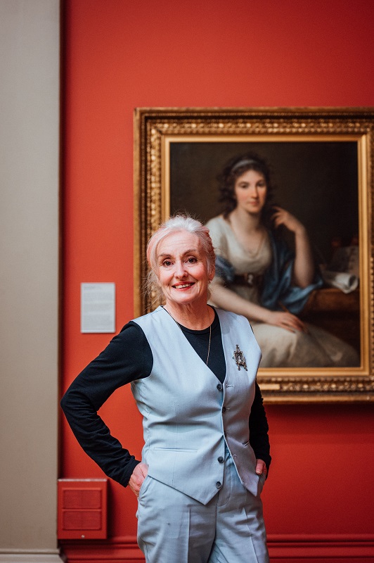 Portrait of Christine with Angelica Kauffman's painting of Ellis Cornelia Knight against a red exhibition wall