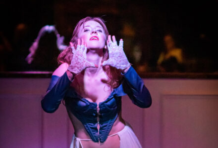 Young woman dressed in a blue corset and lace gloves. The hands in front of the face in a gesture of appeal and red hair. In the background of the spectators.