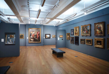 view of Dutch style paintings hung in a salon style exhibition space