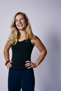 Portrait of yoga instructor jess, a white woman with long blonde hair with her hands on her hips, smiling at the camera