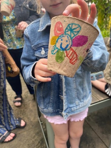 a little girl wearing a denim jacket and pink shorts shows a recyclable vase with a smiling flower drawn on it in her room