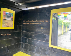 internal view of the pocket park hut. on the right portion of the mirror and on the left a notice board. at the bottom part of the yellow bench