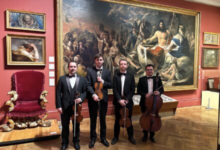 four string musicians holding their instruments, standing in front of a wall painting depicting Greek Gods, in Manchester Art Gallery