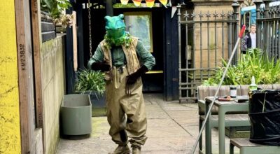 a man in a green frog mask is walking and lceaning the sidewalk